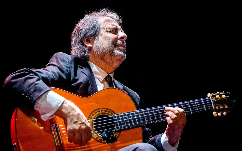 A seated guitarist playing a Spanish guitar